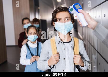 Lehrer mit berührungslosen Thermometer auf Schüler in medizinische Maske In der Schule Stockfoto