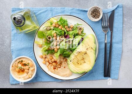 Kichererbsen-Avocado-Salat auf einem Teller, gesunder veganer vegetarischer Salat mit Hummus, Grüns, Kichererbsen und großer Avocado, die zur Hälfte in Scheiben geschnitten sind. Draufsicht Stockfoto