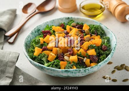 Herbstsalat mit Grünkohl, geröstetem Kürbis, Samen und getrockneten Preiselbeeren in einer Schüssel. Grauer Hintergrund. Modell. Draufsicht. Stockfoto