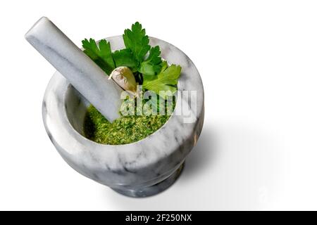 Grüne Sauce in Marmormörtel und Stößel mit Petersilie, Knoblauch und nativem Olivenöl extra. Piemontesische Sauce, Italien, in der Ansicht von oben isoliert auf weiß Stockfoto