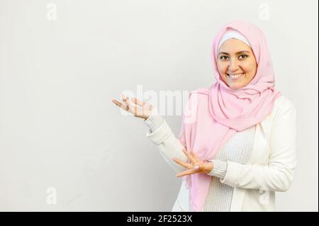 Junge hübsche muslimische arabische Frau in rosa Hijab stehend isoliert über dem grauen Hintergrund und präsentiert zeigen mit den Händen auf den leeren Raum für Werbung, Mockup Bild für Gesundheitswesen Konzept, Stockfoto