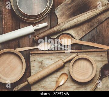 Vintage-Artikel aus der Holzküche: Sieb, Nudelholz, leere Löffel und runde Teller auf braunem Holztisch Stockfoto