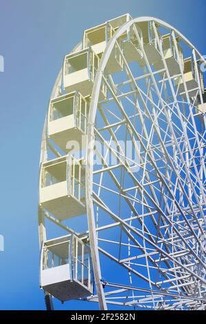 Modernes weißes Riesenrad mit geschlossenen Glaskabinen vor blauem Himmel in der Sonne. Tourismuskonzept. Stockfoto