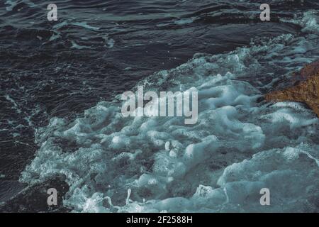 Am Strand am Abend krachen Wellen auf den Felsen. Spezieller grüner Filter. Stockfoto