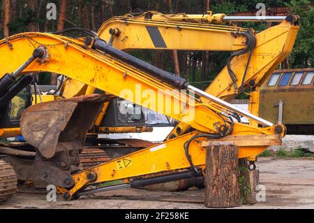 Der alte kaputte Bagger wird repariert. Rostiges Metall, Reste von alter gelber Farbe, ein zerbrochener Eimer. Reparaturbereich. Reparaturkonzept für Baumaschinen Stockfoto