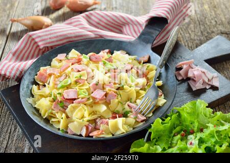 Österreichische Schinkenfleckerl, serviert in einer eisernen Pfanne mit grünem Beilagensalat Stockfoto