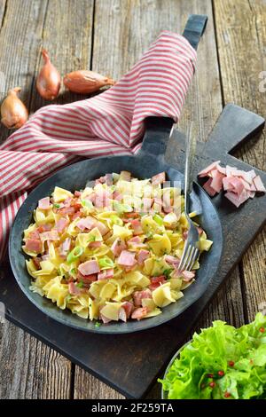 Österreichische Schinkenfleckerl, serviert in einer eisernen Pfanne mit grünem Beilagensalat Stockfoto