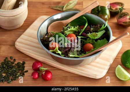 Salat aus grünen Sprossen, Salat, Spinat, Kirschtomate, Samen, Rettich, Kalk und Lorbeerblättern, serviert in einer Metallschale auf einem hölzernen Schneidebrett auf einer res Stockfoto