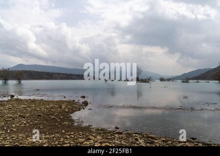 Ein Bergsee und Stausee mit Treibholz und toten Bäumen Und eine Berglandschaft dahinter Stockfoto