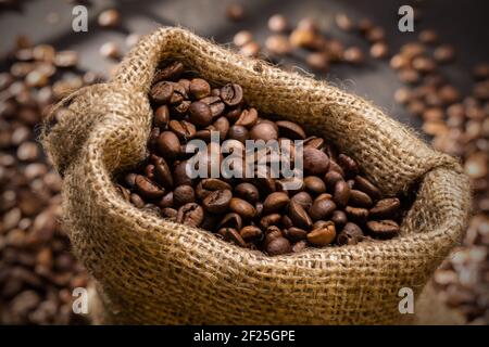 verschüttete Kaffeebohnen in Tasche am Holztisch. Morgenlicht Stockfoto