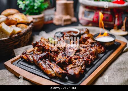 Seitenansicht Fleischkebab mit gegrillten Kartoffeln und Gemüse mit Soße und Feuer auf einem Brett Stockfoto