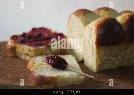 Frisch gebackener Brioche-Brötchen-Laib in Scheiben geschnitten und auf einem Holzbrett aufbewahrt. Serviert mit Marmelade. Aufnahme auf weißem Hintergrund. Stockfoto