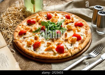 Seitenansicht Pizza mit Garnelen und Champignons Tomaten und Rucola Und mit einem alkoholfreien Getränk Stockfoto