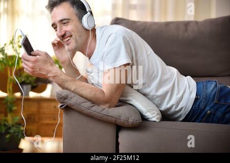 Glücklicher Mann, der ein Handy benutzt, um Musik zu hören Ein Sofa zu Hause Stockfoto