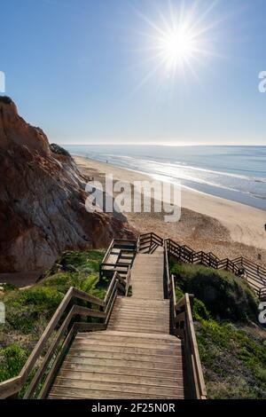 Eine lange Holzpromenade Zugang zum Strand führt hinunter zu einem Breiter goldener Strand mit bunten Sandklippen Stockfoto