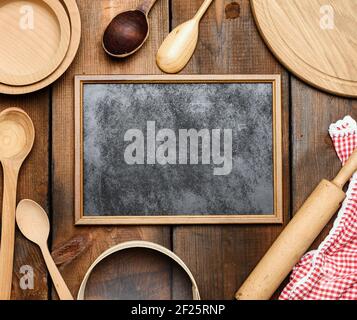 Leerer schwarzer Rahmen und Vintage-Artikel aus Holz in der Küche: Sieb, Nudelholz, leere Löffel und runde Teller Stockfoto
