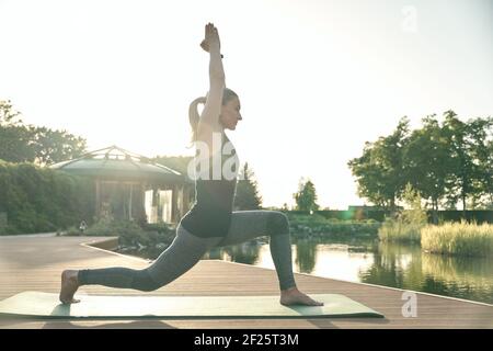 Verbessern Sie sich. In voller Länge Aufnahme einer entspannten Frau, die in Yoga-Pose steht, während sie Yoga auf einer Matte in der Natur macht Stockfoto