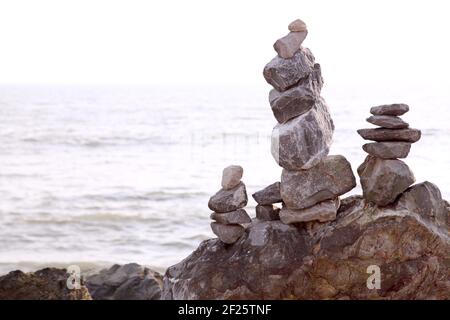 Kunst, Disziplin oder Hobby des Balancierens von Steinen oder Stapeln von Felsen zu Stein oder Stein cairns zu machen. Ausgewogen / gestapelt am Strand mit Meer dahinter. Stockfoto