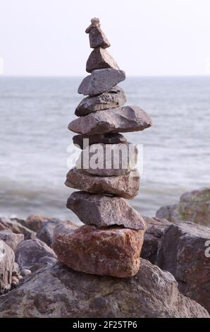 Steinhaufen oder gestapelte Felsen, die am Strand balancieren Oder Küstenlinie mit Meer hinter Stockfoto
