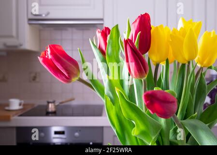 Ein Bouquet aus schönen gelben und roten Tulpen steht auf dem Tisch in einer gemütlichen Küche. Stockfoto