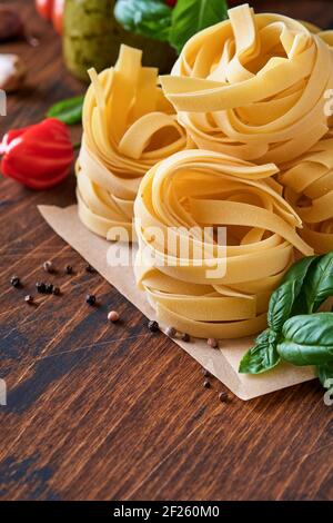 Hausgemachte Tagliatelle Pasta in braunem Papier auf weißem Hintergrund mit Olivenöl, Sause Pesto, Basilikum und Knoblauch auf hellem Tischhintergrund. Stockfoto