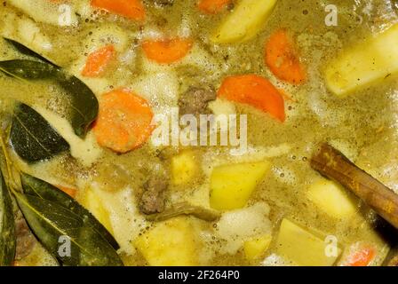 Rindereintopf, der in einem Topf auf einem Herd von direkt oben gesehen köchelt. Bay Blätter sichtbar mit gemischtem Gemüse und Holzlöffel mit Kopieplatz. Stockfoto