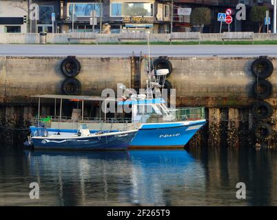 Zwei kleine Fischerboote, die im Dock von Maliano festgemacht sind Ebbe mit der Marina Cafe Bar in der Straße Hinter Santander Cantabria Spanien am frühen Morgen Stockfoto