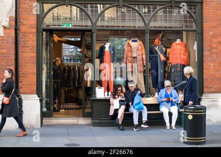 London, Großbritannien - 20. September 2020, Leute mit Einkaufen nach dem Einkaufen sitzen vor dem Geschäft auf Covent Garden. Stockfoto