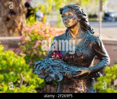 Bronzestatue einer Frau, die Blumen in einem Garten im Freien hält. Stockfoto