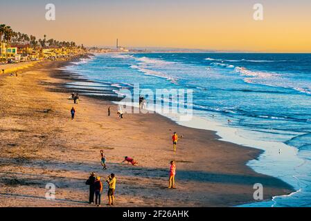 Touristen, die am Strand in der späten Nachmittagssonne spielen, Wellen am Meer und Strandgrundstück. Stockfoto