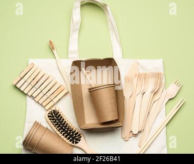 Weiße Stofftasche und Einweggeschirr aus braunem Bastelpapier Auf einem grünen Hintergrund Stockfoto