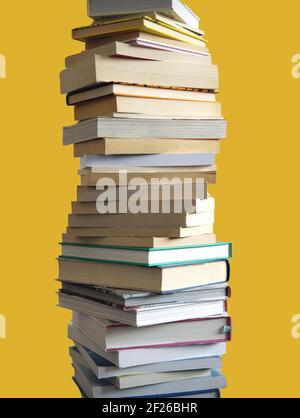 Ein hoher Stapel von vielen Büchern, die hoch, isoliert auf gelb angehäuft sind Stockfoto