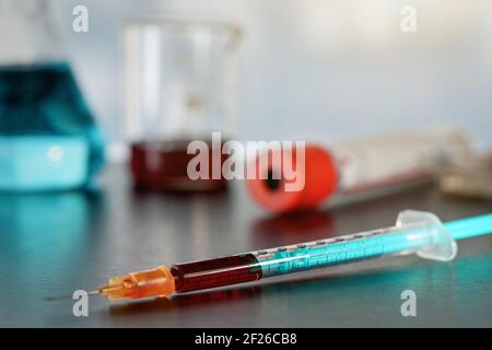 Hypodermische Spritzennadel gefüllt mit dunkelrotem Blut auf schwarzem Tisch, verschwommener Hintergrund für Laborgeräte Stockfoto