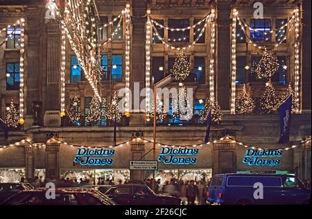 Historische 1985 Archiv Nachtansicht von Dickins & Jones hoch Qualitäts-Kaufhaus mit Gebäude Shop Front und dekoriert Weihnachten Bäume eingeschaltet Beleuchtung im berühmten Regent Street West End Einkaufsviertel unvermeidlich 1980s Stau & Bürgersteig Massen Käufer beleuchteten das Logo der Handelsmarke über jedem Fenster in Ein Archivbild aus dem Jahr 80s von der Art und Weise, wie wir uns befanden Weihnachten in London England Stockfoto