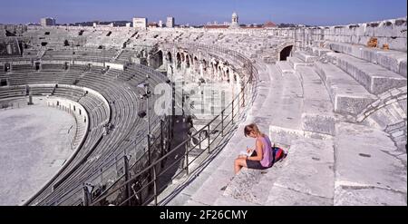 Historikal1990s Archiv Innenansicht der erhaltenen französischen Arena von Nîmes ein berühmtes Amphitheater aus dem Römischen Reich, das 1993 besichtigt wurde Von der höchsten Ebene mit jungen Frau Touristen sitzen auf Steinterrasse mit Blick auf die Innenansicht der 90er Jahre bis hin zur Funktionsfähigkeit Veranstaltungsarena und niedrigere Ebenen der Sitzgelegenheiten auf einem heißen Blauer Himmel Sonnenschein Tag in einem Archivbild Reise in Das Departement Gard der Region von Südfrankreich Stockfoto