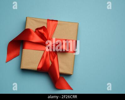 Quadratische Geschenkbox ist in rotem Papier verpackt und gewelltes rotes Seidenband, festlicher Hintergrund Stockfoto