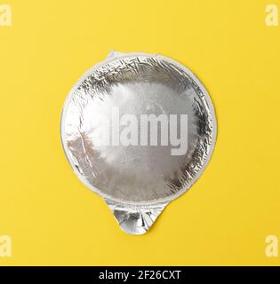 Runder, dünner Aluminiumdeckel für Joghurtgläser aus Kunststoff auf einem Gelber Hintergrund Stockfoto