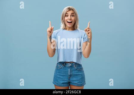 Die Taille-up-Aufnahme der begeisterten kreativen blonden Frau in trendy beeindruckt Sommer-Outfit lächelnd keuchend bezaubert und begeistert Stockfoto