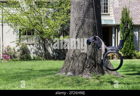 Eine niedliche Pferdeschaukel aus einem Gummireifen An einem Baum vor einem bemalten Ziegel hängen Haus mit Landschaftsgestaltung in einer gehobenen Nachbarschaft Stockfoto