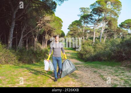 Ehrenamtlicher Mann mit Müllbeutel, der den Wald aus Plastik säubert Verschmutzung Stockfoto