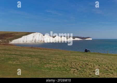 SEAFORD, SUSSEX/UK - APRIL 5 : Mann sitzt auf einer Bank mit Blick auf die Seven Sisters in der Nähe von Seaford in Sussex am 5. April 2018. Uni Stockfoto