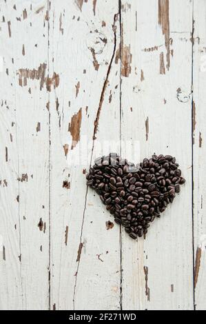 Draufsicht auf Herz Symbol aus gerösteten Kaffeebohnen auf einem rustikalen offweißen Holztisch. Herzförmige Kaffeebohnen. Kreatives Flat Lay-Konzept für die Liebe Stockfoto