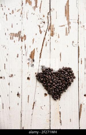 Draufsicht auf Herz Symbol aus gerösteten Kaffeebohnen mit einem Stück fehlt auf einem rustikalen weißen Holztisch. Herzförmige Kaffeebohnen. Kreative flache Laie. Stockfoto