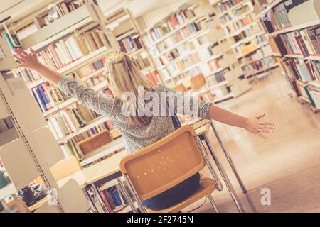 Lernen für Prüfungen: Müde Studentin in der Universitätsbibliothek, Bücherhaufen Stockfoto