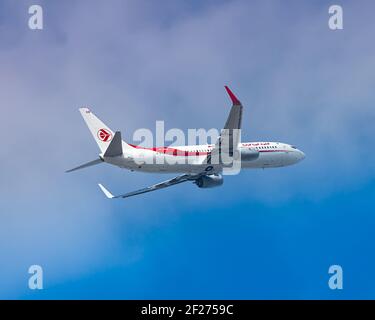 London, Heathrow Airport - Mai 2019: Air Algérie Boeing 737, fliegt durch einen strahlend blauen Himmel mit trüben Wolken. Das Flugzeug geht nach links. imag Stockfoto