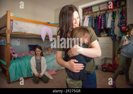 Mama umarmt ein weinendes Kleinkind, während Schwestern auf schauen. Stockfoto