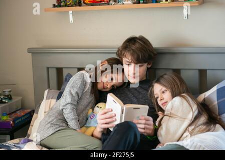 Tween junge Lesung zu seinen kleinen Schwestern im Schlafzimmer. Stockfoto