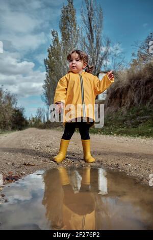 Ein 2-jähriges Mädchen, das neben einem Schlamm reflektiert Pfütze Stockfoto