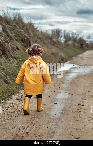 Ein zweijähriges Mädchen in einem gelben Regenmantel beim Gehen In einen Schlamm pudd Stockfoto