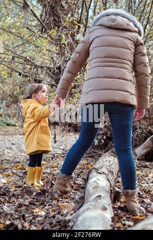 Eine Mutter hilft ihrer kleinen Tochter, über einen zu gehen Protokoll Stockfoto